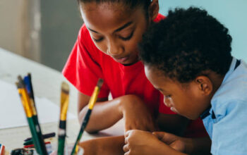 Closeup of elementary African American kids creatively drawing and painting with brushes and crayon - children creative education concept
